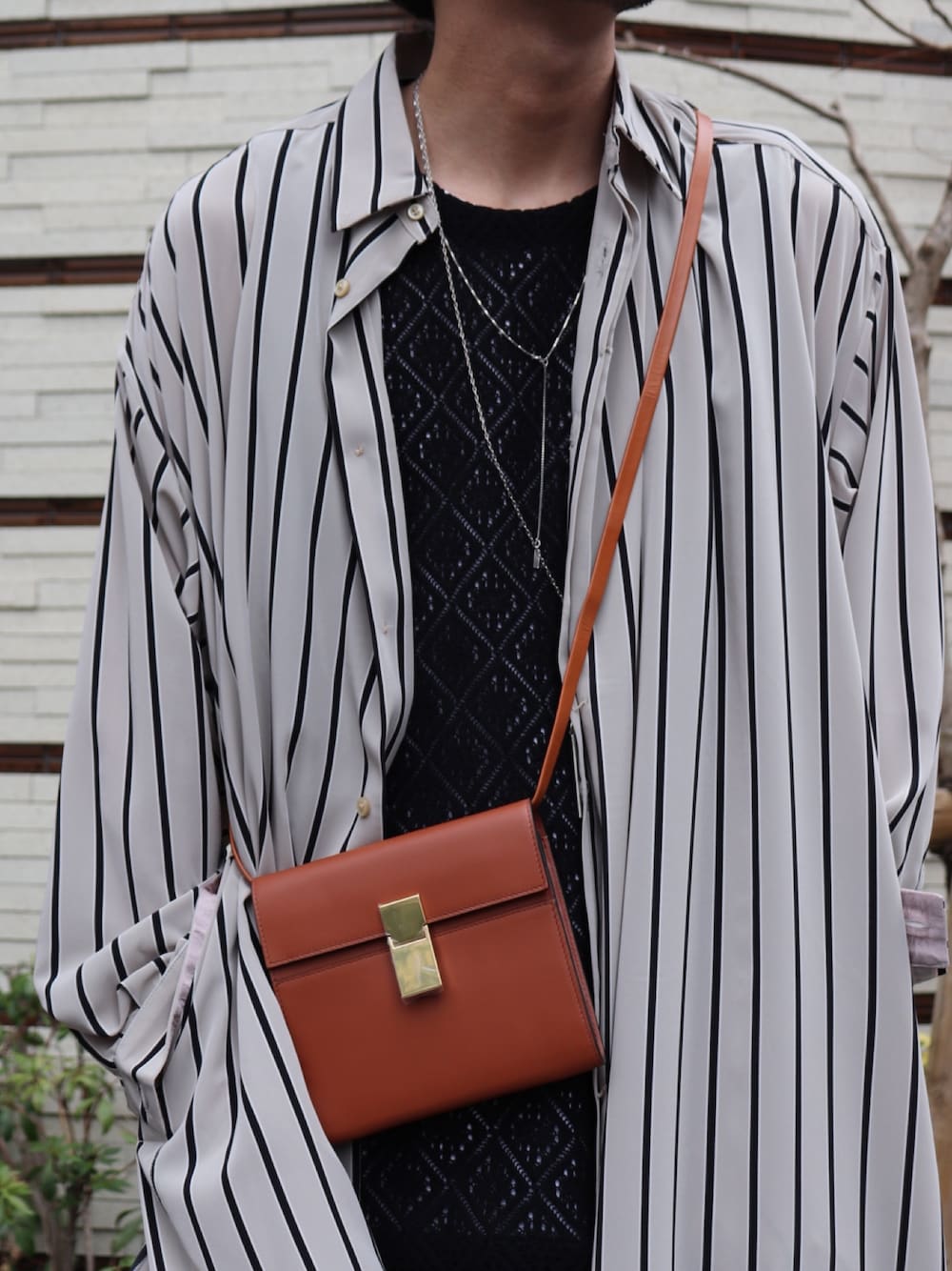 ブラウン系のショルダーバッグ、ブラック系のトップス、ブラック系のスラックスを着用したメンズの春コーディネートの2枚目の写真