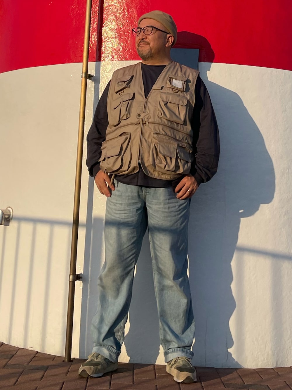 ブルー系のデニムパンツ、ベージュ系のベスト、ベージュ系のスニーカーを着用したメンズの秋コーディネートの1枚目の写真