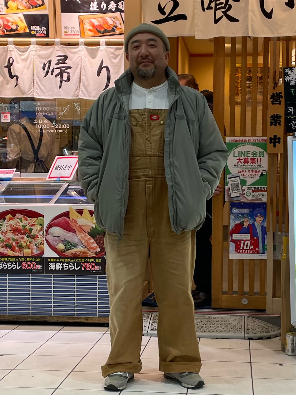 グレー系のミリタリージャケット、ブラウン系のサロペット/オーバーオール、グレー系のスニーカーを着用したメンズの冬コーディネートの1枚目の写真