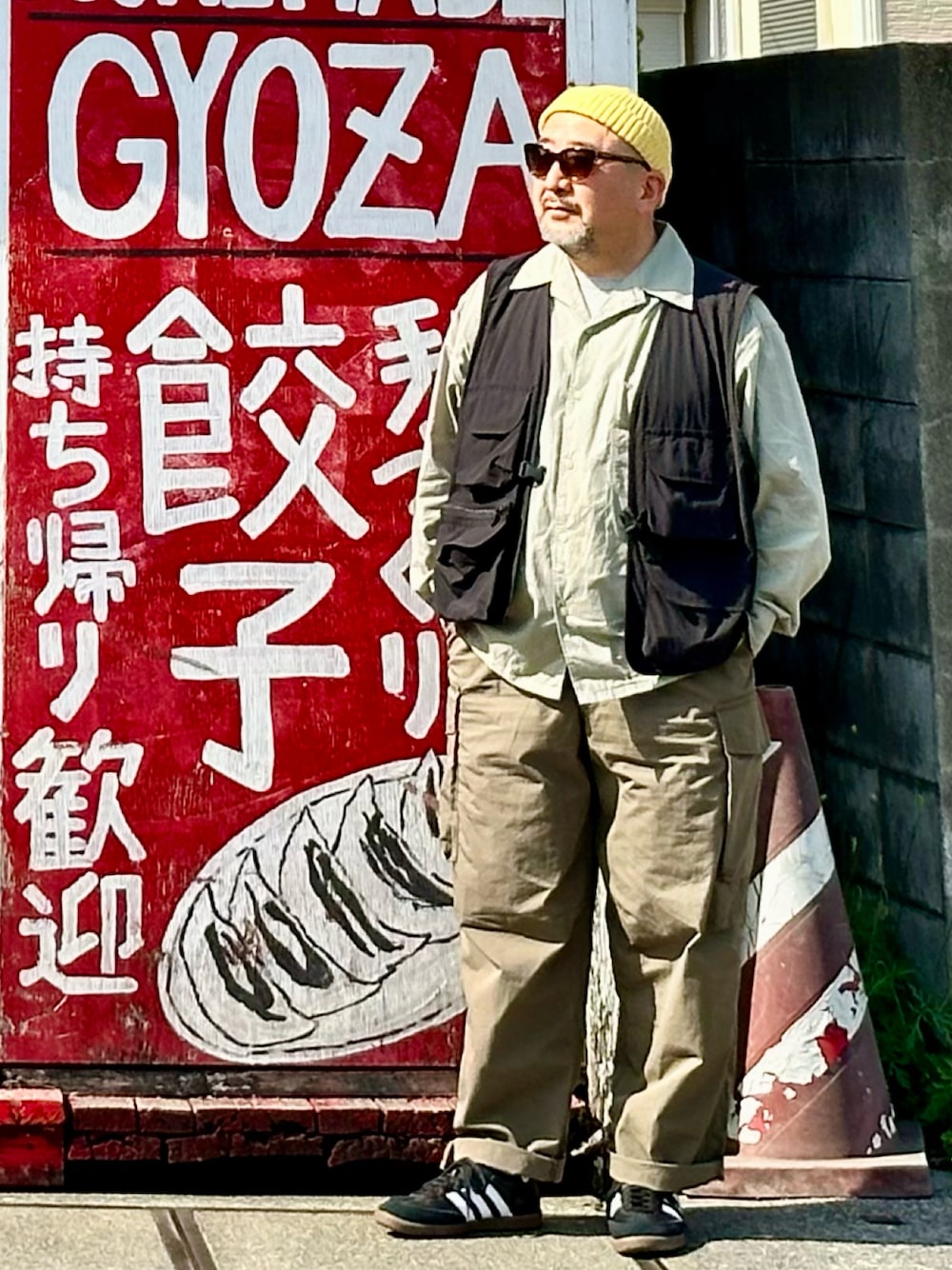 グリーン系のカーゴパンツ、ブラック系のベスト、ブラック系のスニーカーを着用したメンズの春コーディネートの1枚目の写真