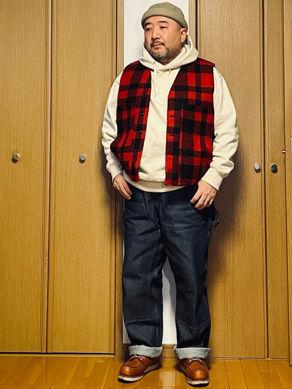 ブルー系のデニムパンツ、ブラウン系のブーツ、レッド系のベストを着用したメンズの春コーディネートの1枚目の写真