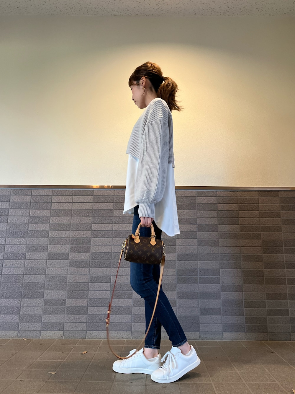 グレー系のニット/セーター、ブラウン系のバッグ、ブルー系のデニムパンツを着用したレディースの冬コーディネートの1枚目の写真