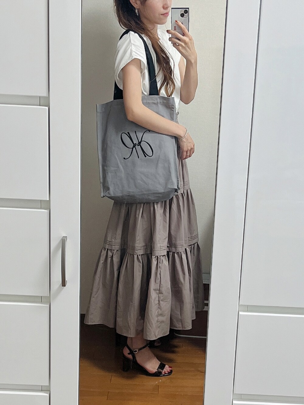 グレー系のトートバッグ、ホワイト系のTシャツ/カットソー、ベージュ系のスカートを着用したレディースの夏コーディネートの1枚目の写真