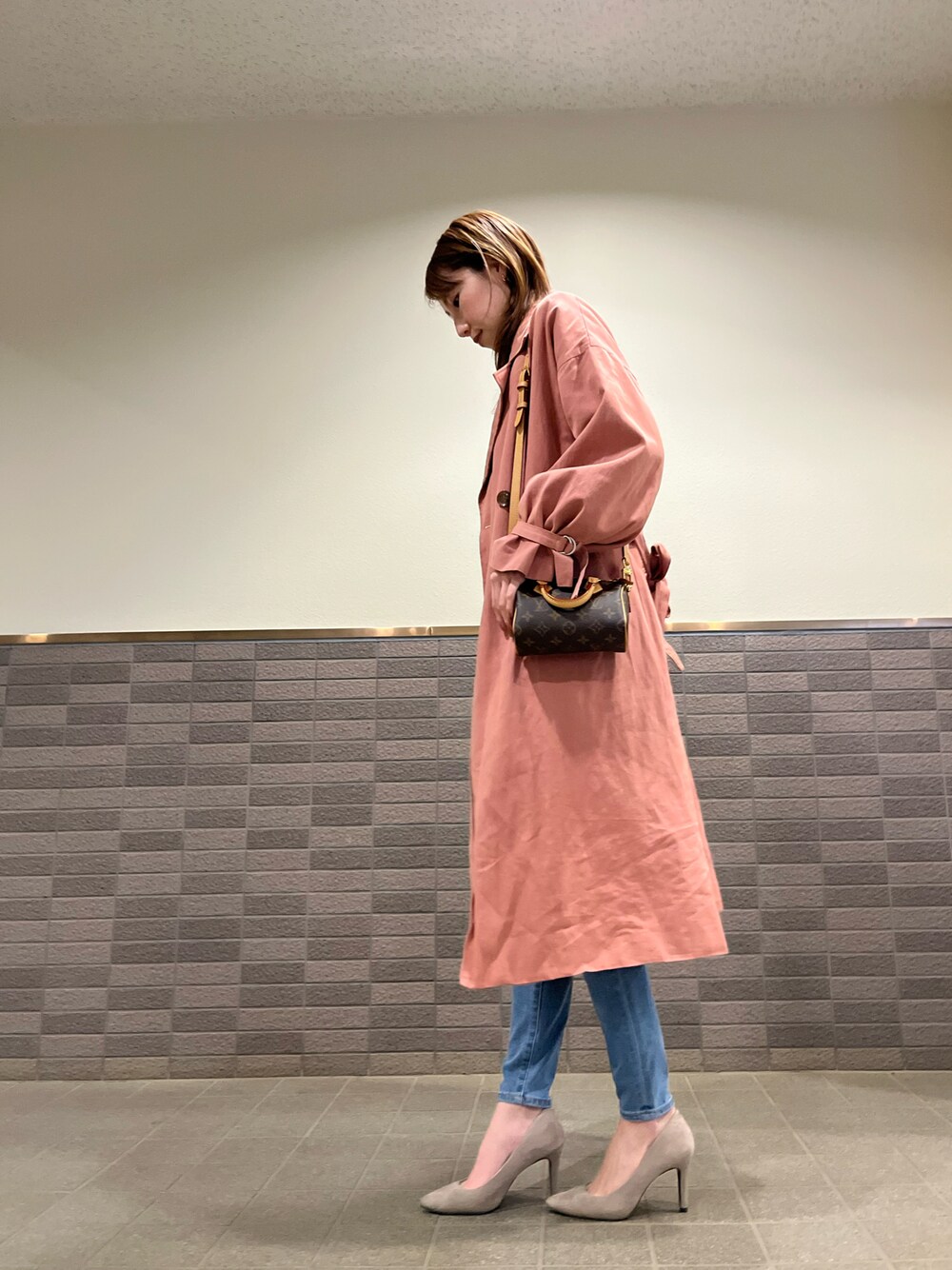 ピンク系のトレンチコート、ブルー系のデニムパンツ、ベージュ系のパンプスを着用したレディースの冬コーディネートの1枚目の写真