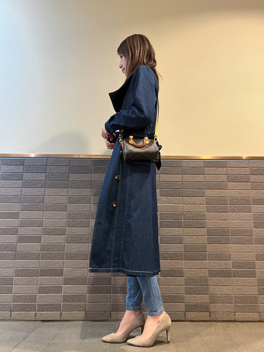 ブラウン系のバッグ、ブルー系のトレンチコート、ブルー系のデニムパンツを着用したレディースの冬コーディネートの1枚目の写真