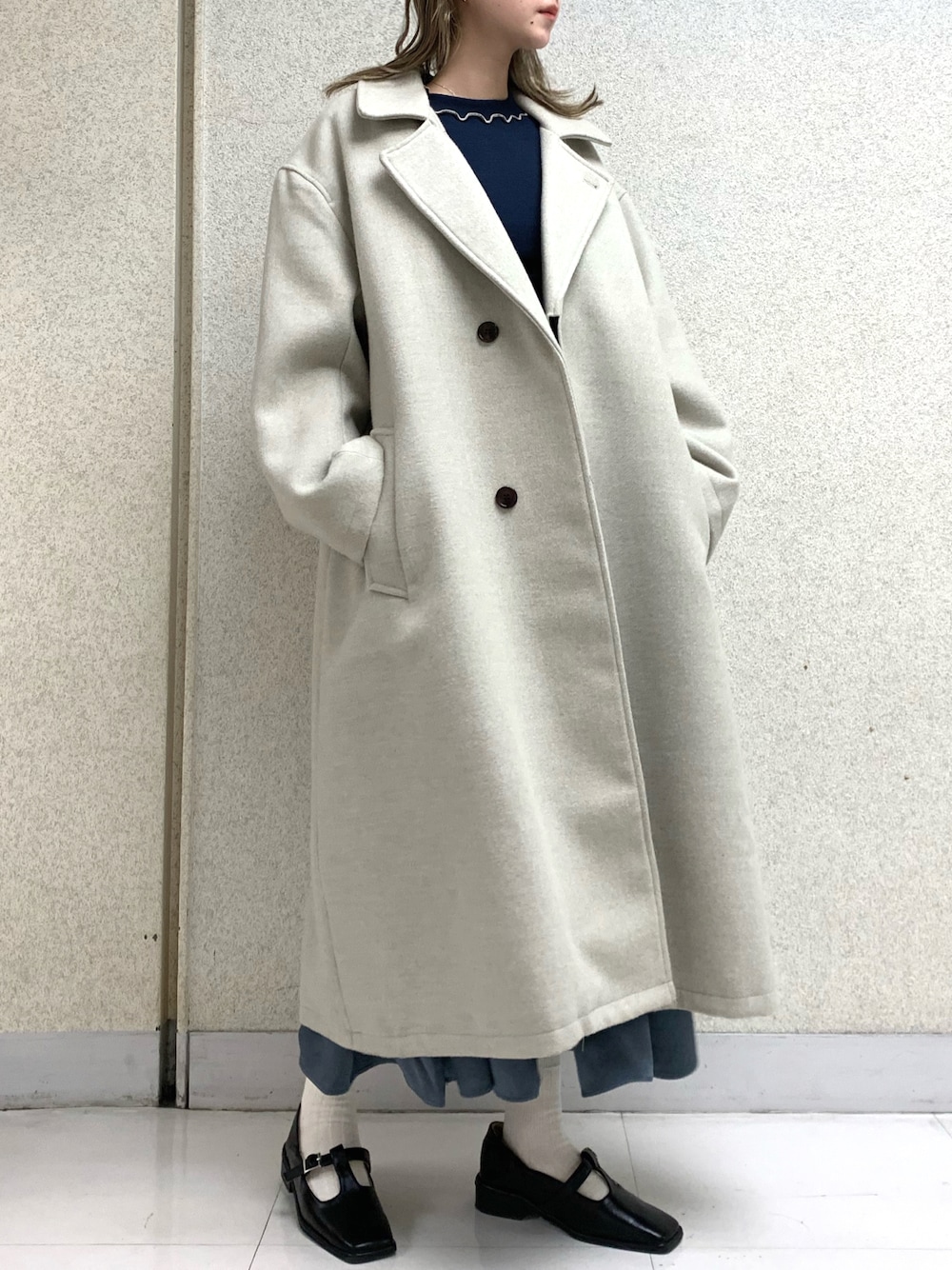 ホワイト系のチェスターコート、ブルー系のスカート、ブルー系のTシャツ/カットソーを着用したレディースの冬コーディネートの1枚目の写真
