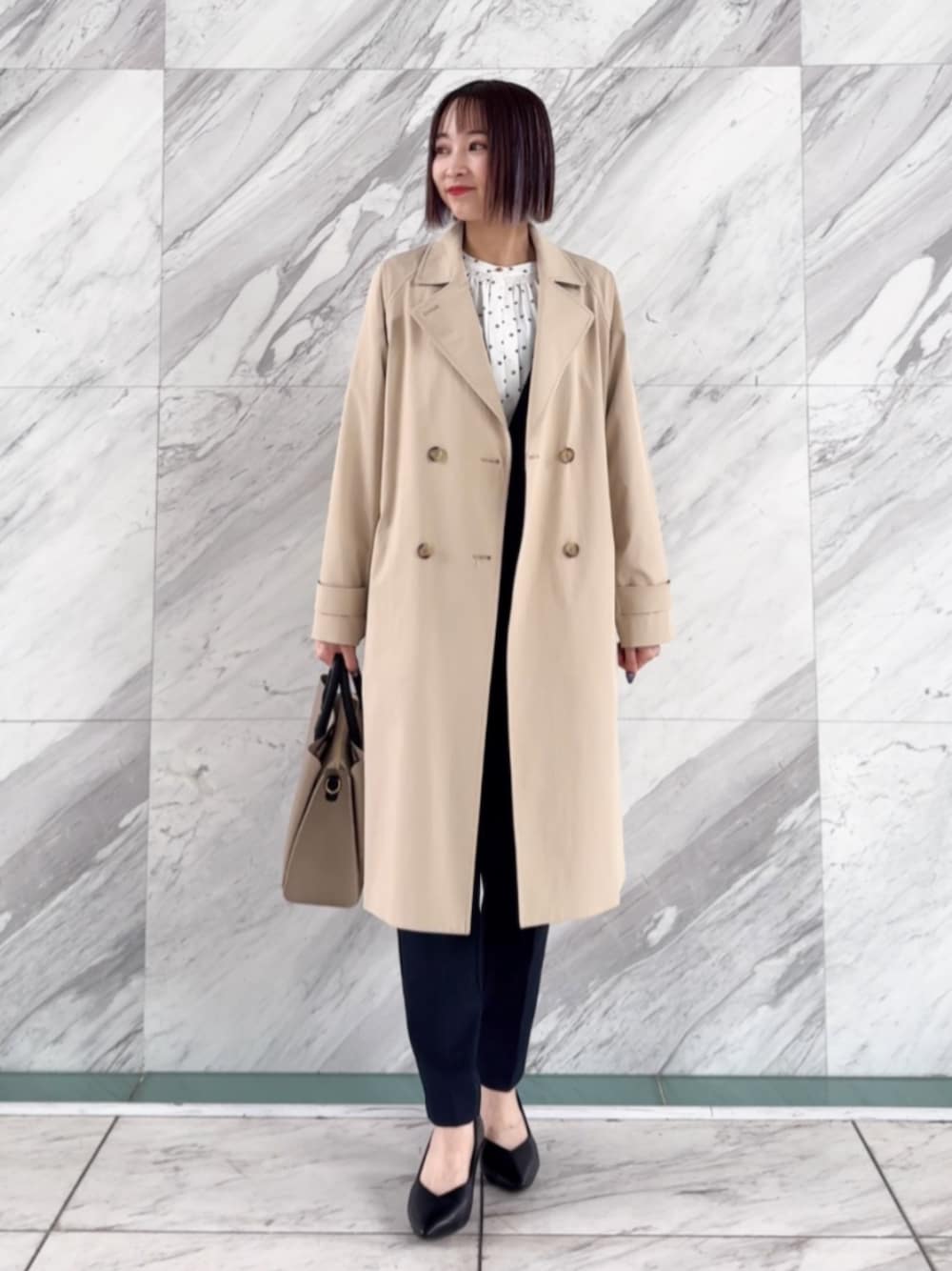 ベージュ系のトレンチコート、ブラック系のパンプス、ブルー系のノーカラージャケットを着用したレディースの春コーディネートの1枚目の写真