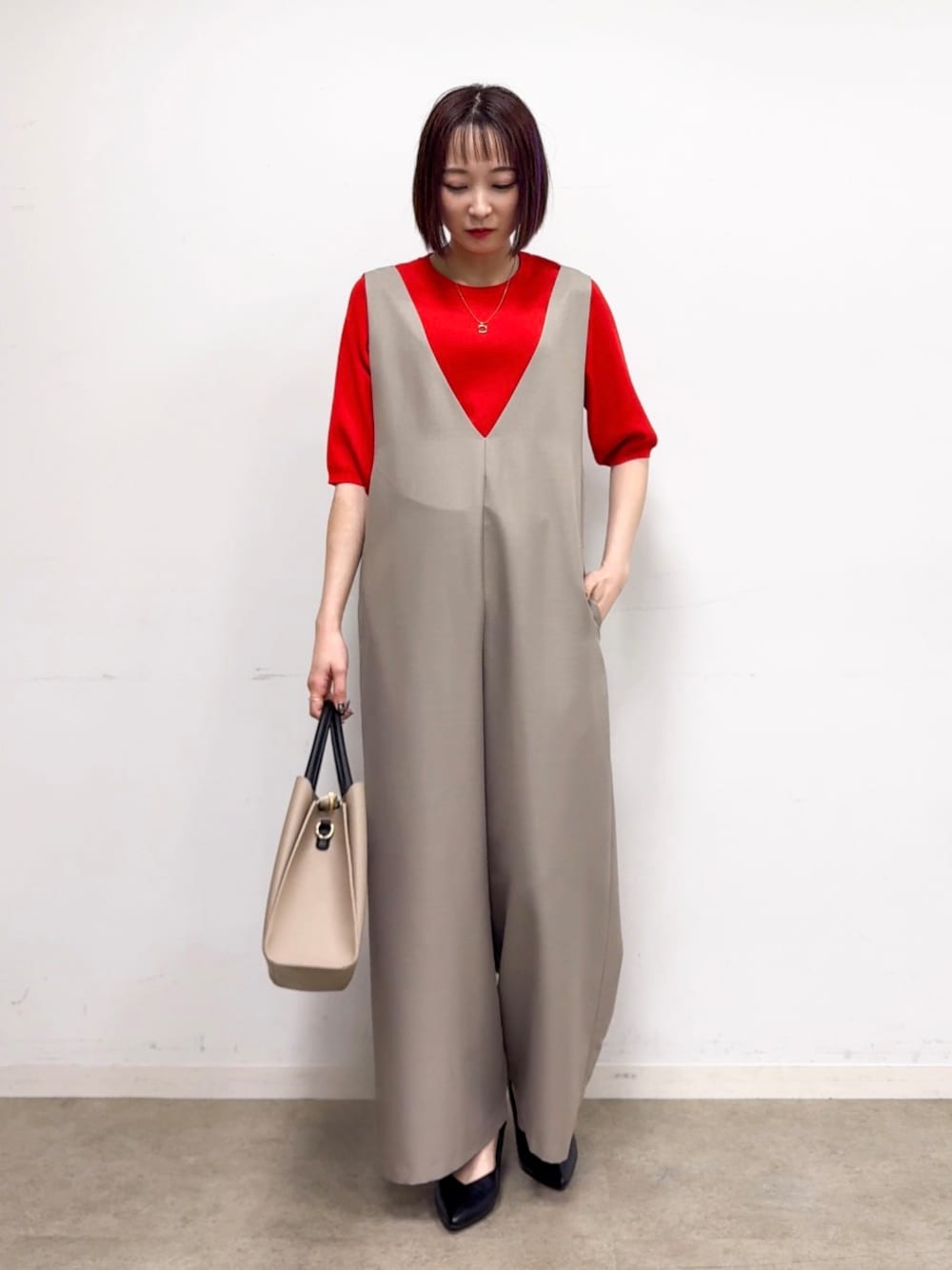 レッド系のニット/セーター、ベージュ系のサロペット/オーバーオール、ブラック系のパンプスを着用したレディースの春コーディネートの1枚目の写真