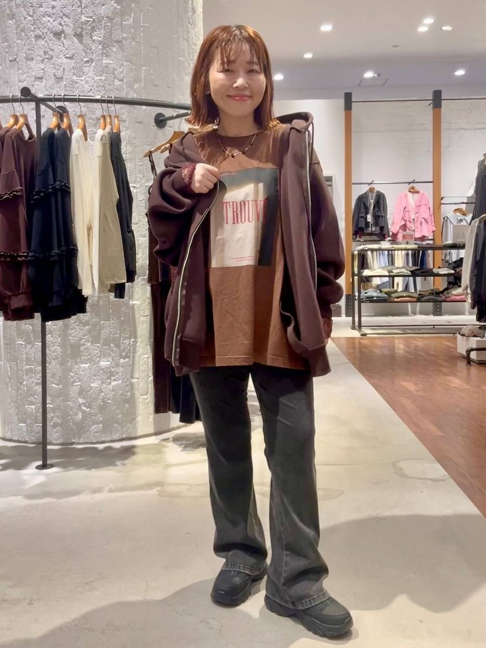 ブラック系のスニーカー、ブラウン系のパーカー、グレー系のデニムパンツを着用したレディースの秋コーディネートの1枚目の写真