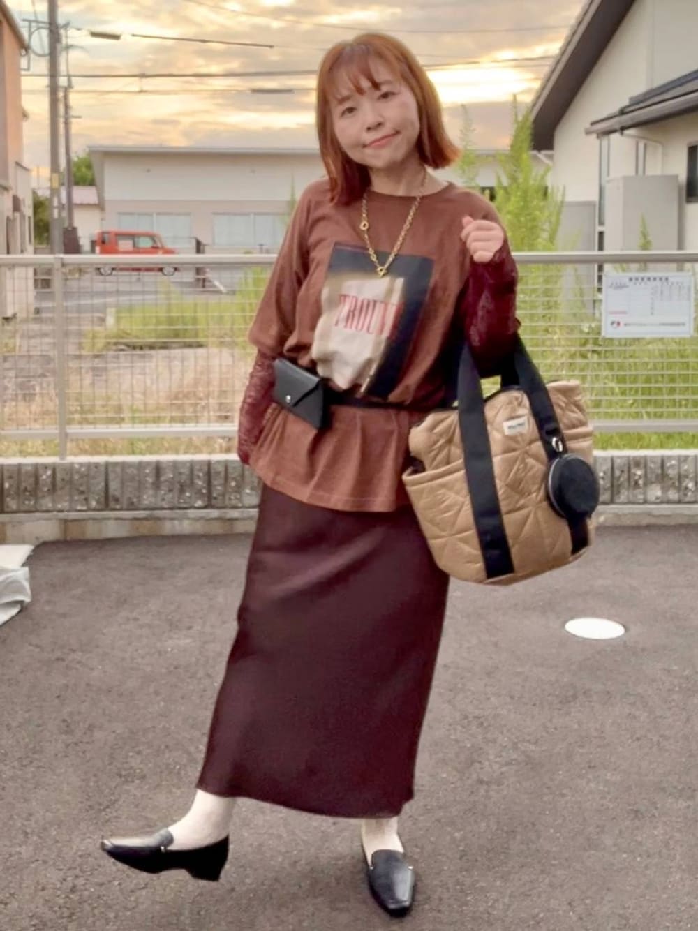 ブラウン系のスカート、ブラウン系のTシャツ/カットソー、ゴールド系のネックレスを着用したレディースの秋コーディネートの1枚目の写真