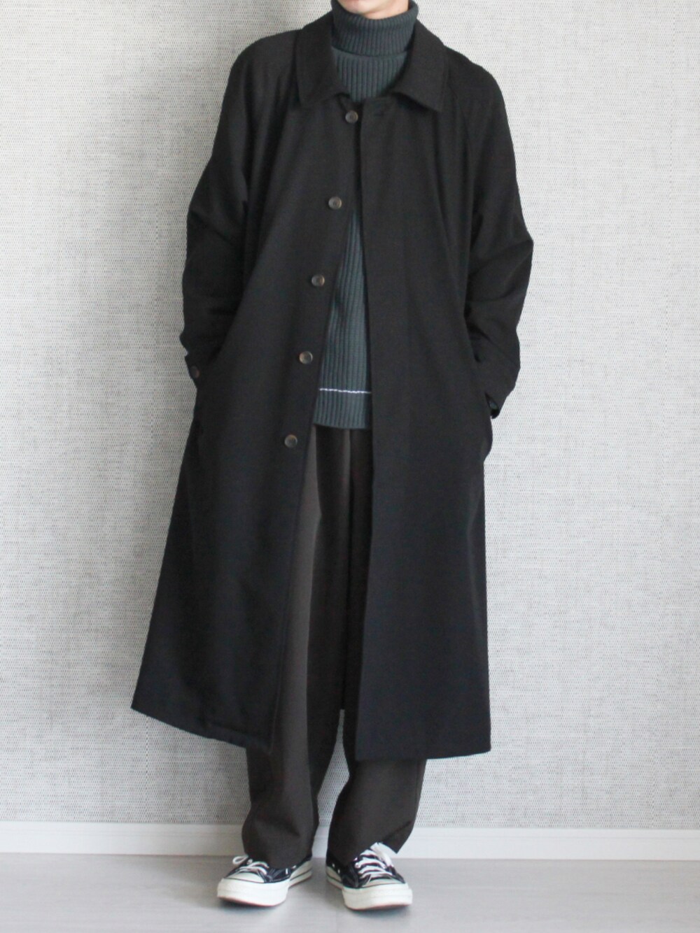 ブラック系のステンカラーコート、グリーン系のニット/セーター、ブラウン系のスラックスを着用したメンズの秋コーディネートの1枚目の写真