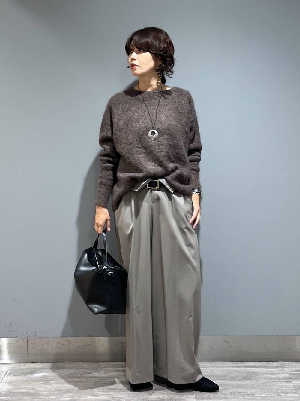 ブラウン系のニット/セーター、ブラック系のショルダーバッグ、ブラック系のブーツを着用したレディースの秋コーディネートの1枚目の写真