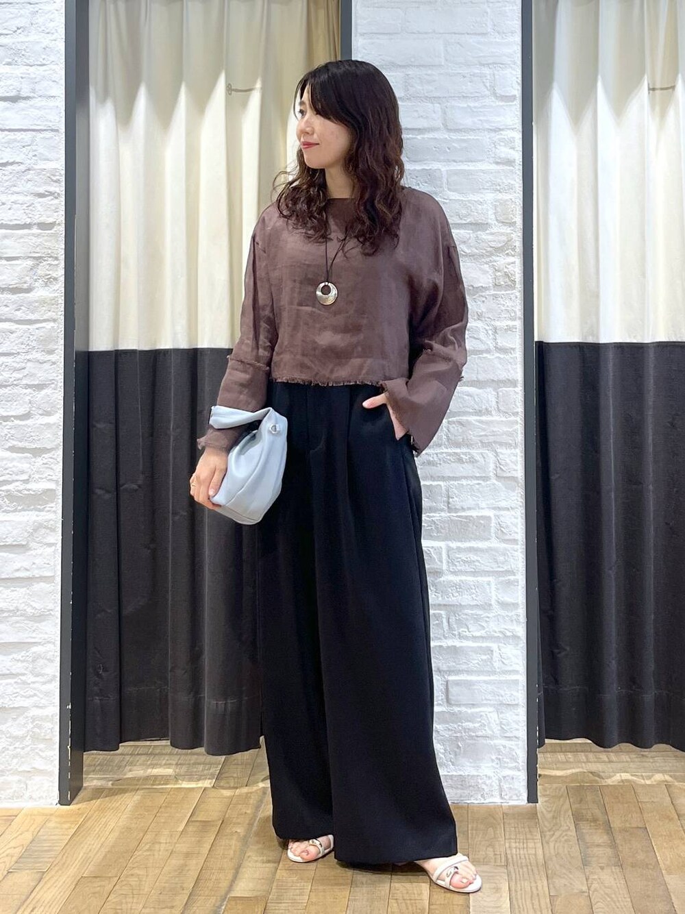 ブルー系のハンドバッグ、ブラウン系のシャツ/ブラウス、ホワイト系のサンダルを着用したレディースの秋コーディネートの1枚目の写真