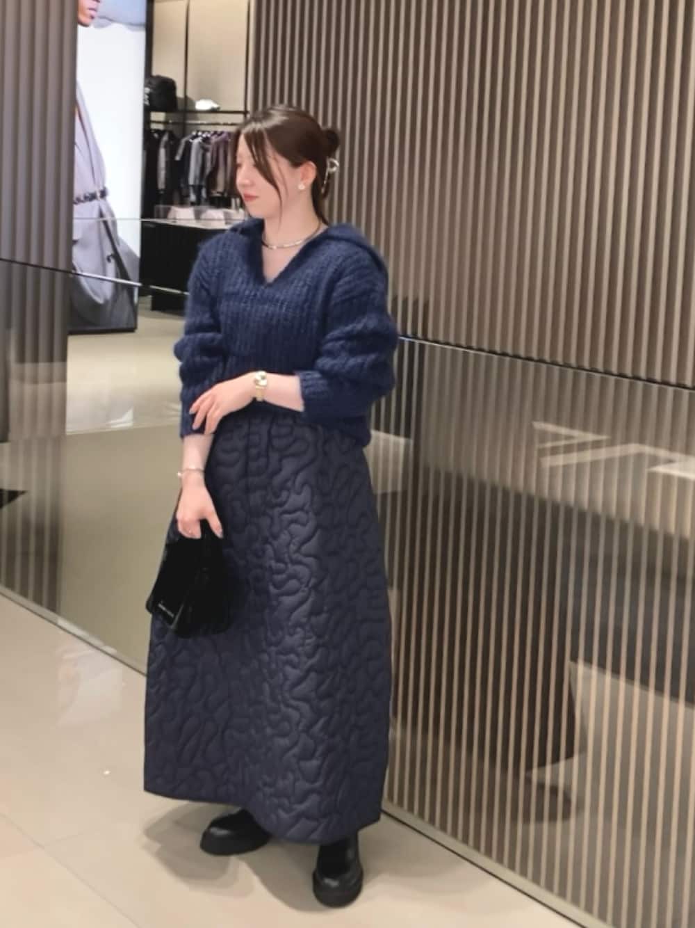 ブルー系のスカート、ブラック系のハンドバッグ、シルバー系のピアス(両耳用)を着用したレディースの秋コーディネートの1枚目の写真