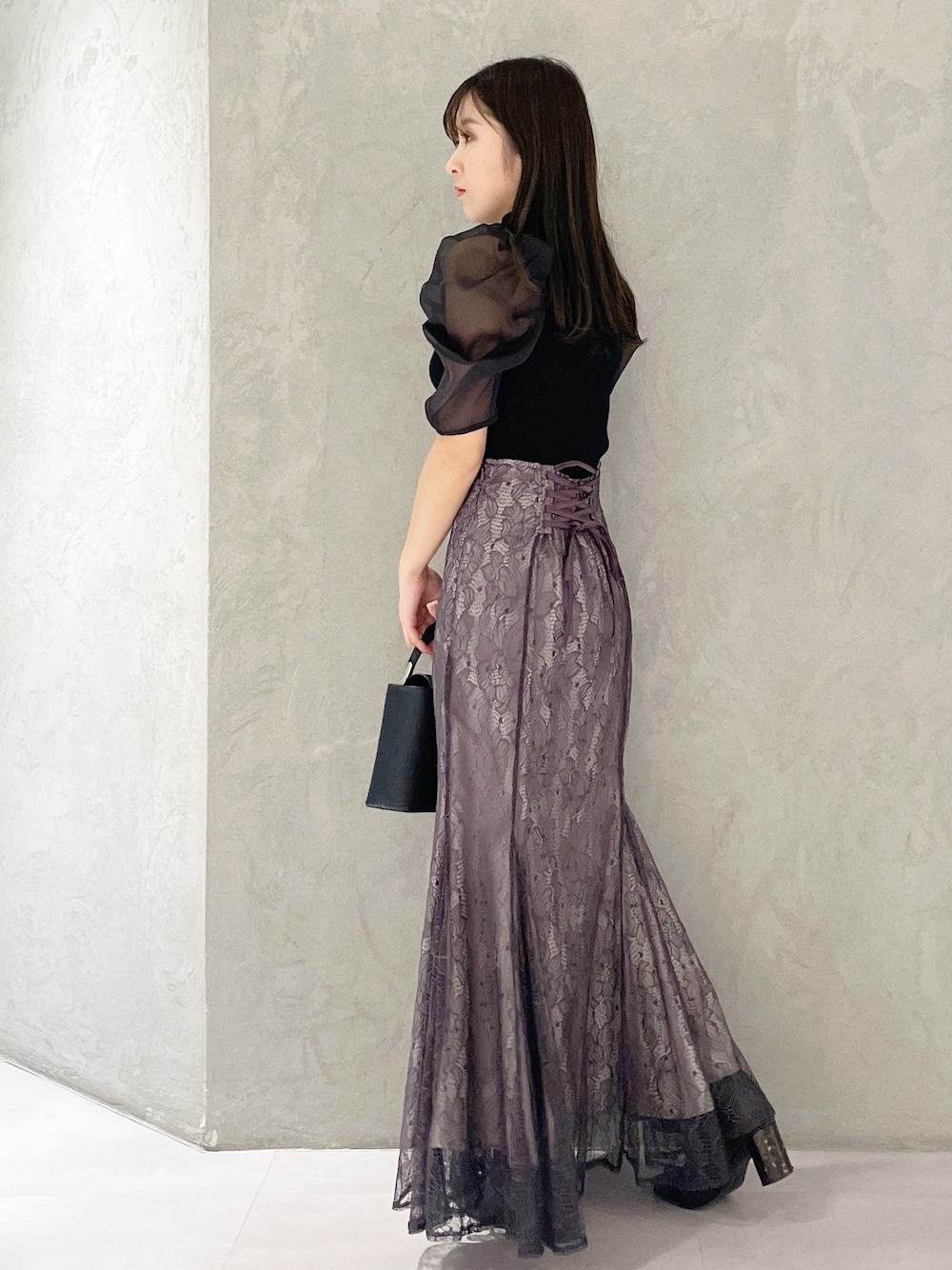 パープル系のスカート、ブラック系のハンドバッグ、ブラック系のニット/セーターを着用したレディースの春コーディネートの1枚目の写真