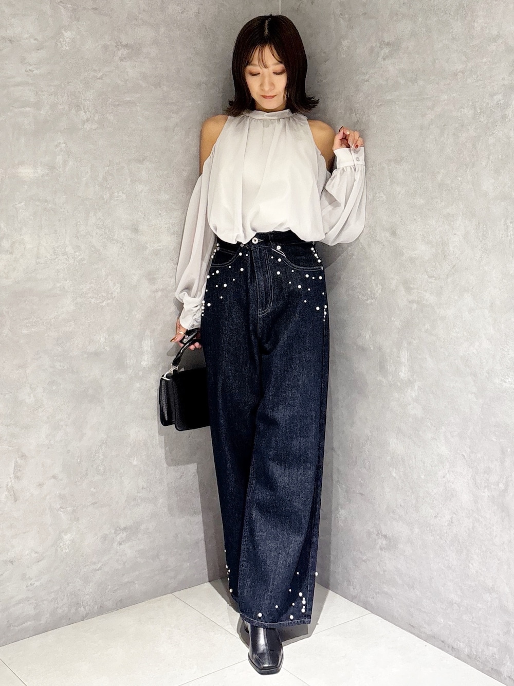 ブルー系のデニムパンツ、ブラック系のブーツ、ブラック系のハンドバッグを着用したレディースの秋コーディネートの1枚目の写真