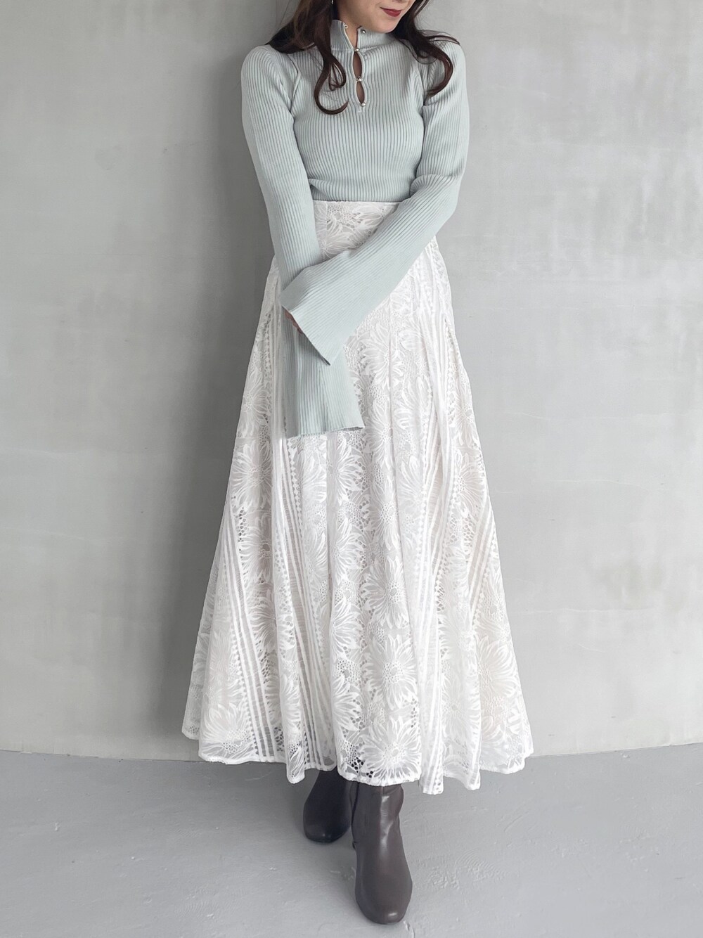 ホワイト系のスカート、グリーン系のニット/セーター、ブラウン系のブーツを着用したレディースの秋コーディネートの1枚目の写真