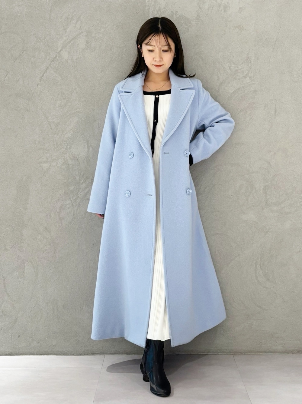 ブルー系のチェスターコート、ブラック系のブーツ、ホワイト系のワンピースを着用したレディースの冬コーディネートの1枚目の写真