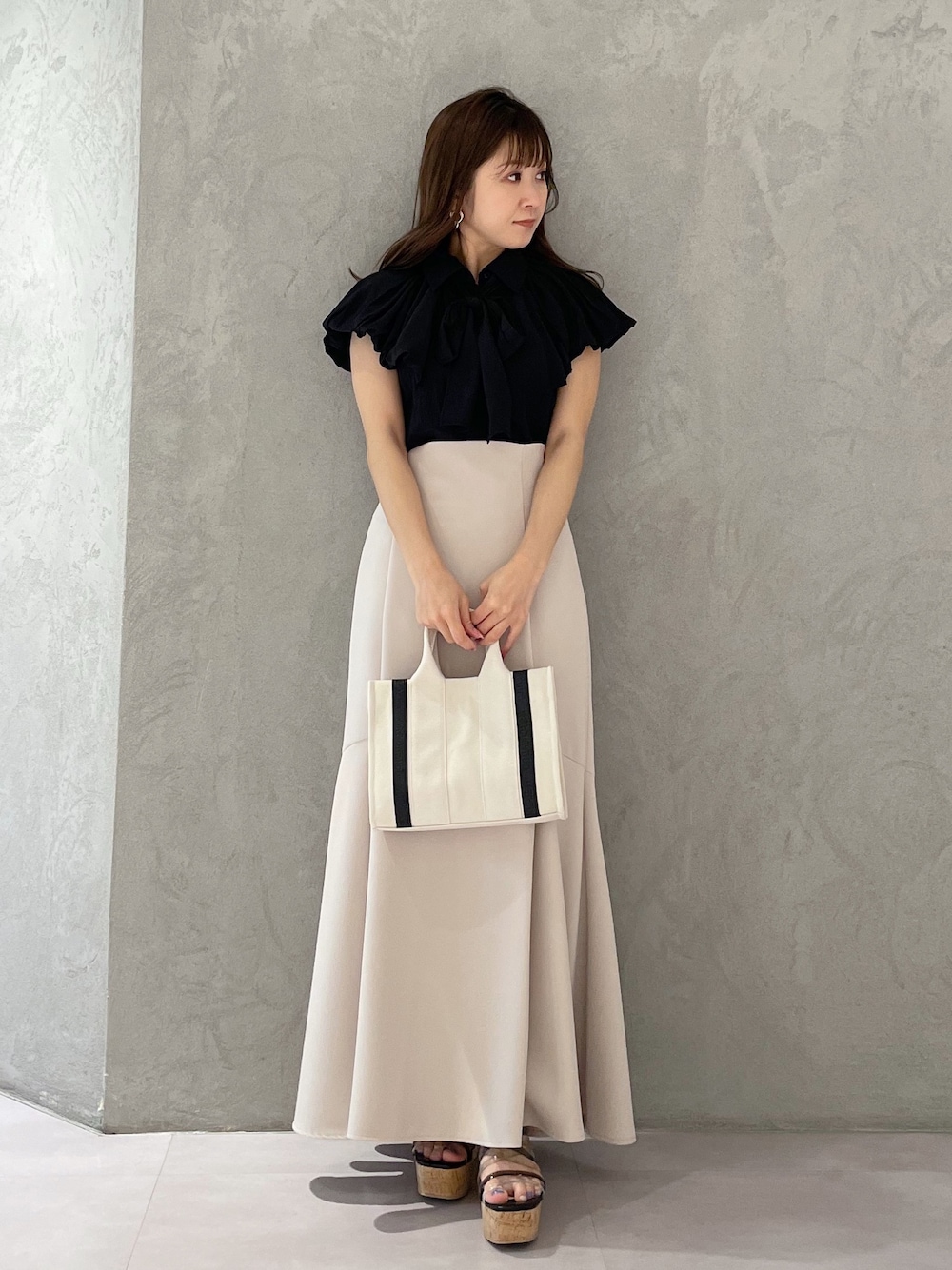 グレー系のハンドバッグ、ベージュ系のスカート、ブラック系のサンダルを着用したレディースの春コーディネートの1枚目の写真