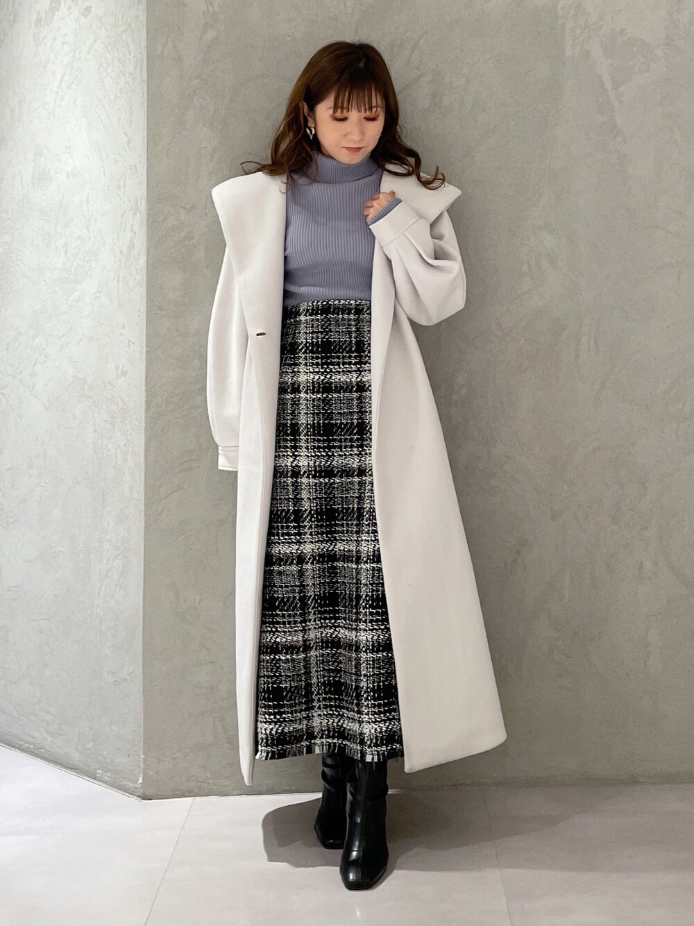 ブルー系のニット/セーター、ブラック系のスカート、ホワイト系のチェスターコートを着用したレディースの冬コーディネートの1枚目の写真