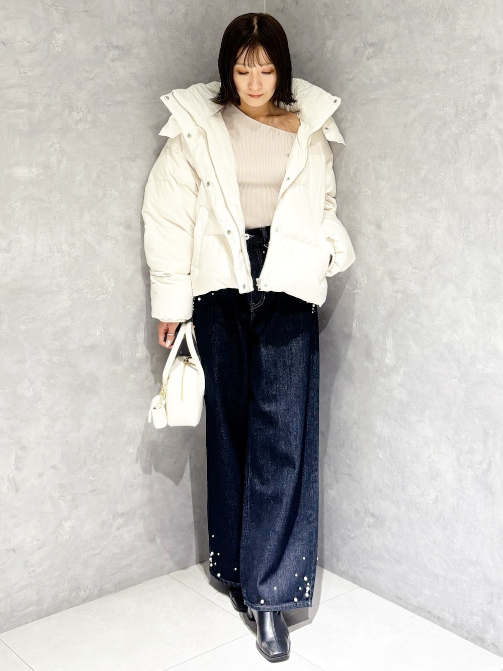 ブルー系のデニムパンツ、ホワイト系のダウンジャケット/コート、ベージュ系のニット/セーターを着用したレディースの秋コーディネートの1枚目の写真