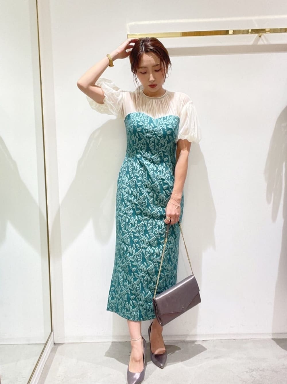 シルバー系のクラッチバッグ、シルバー系のパンプス、グリーン系のドレスを着用したレディースの秋コーディネートの1枚目の写真