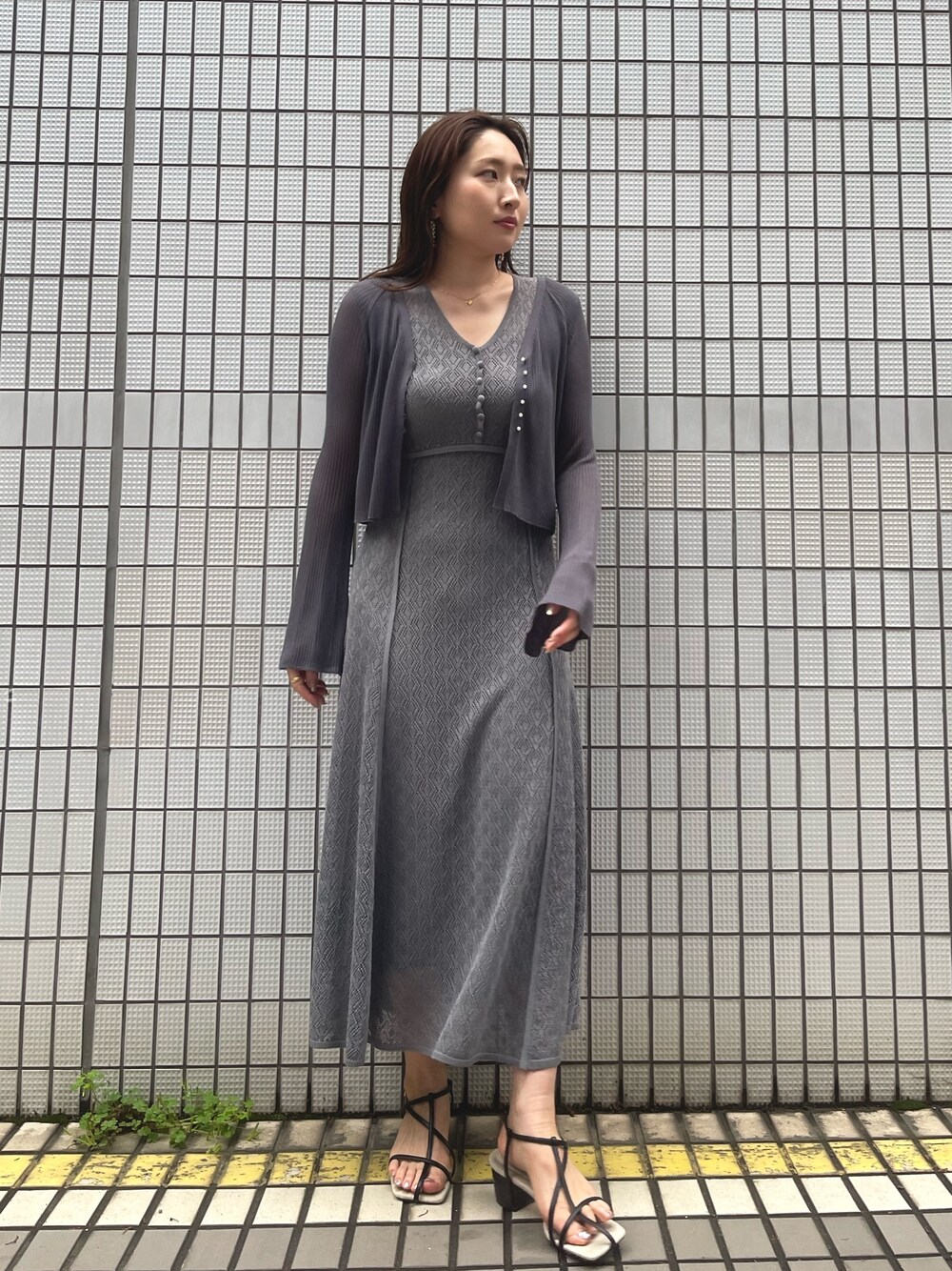 グレー系のワンピース、ブラック系のサンダル、グレー系のカーディガン/ボレロを着用したレディースの春コーディネートの1枚目の写真