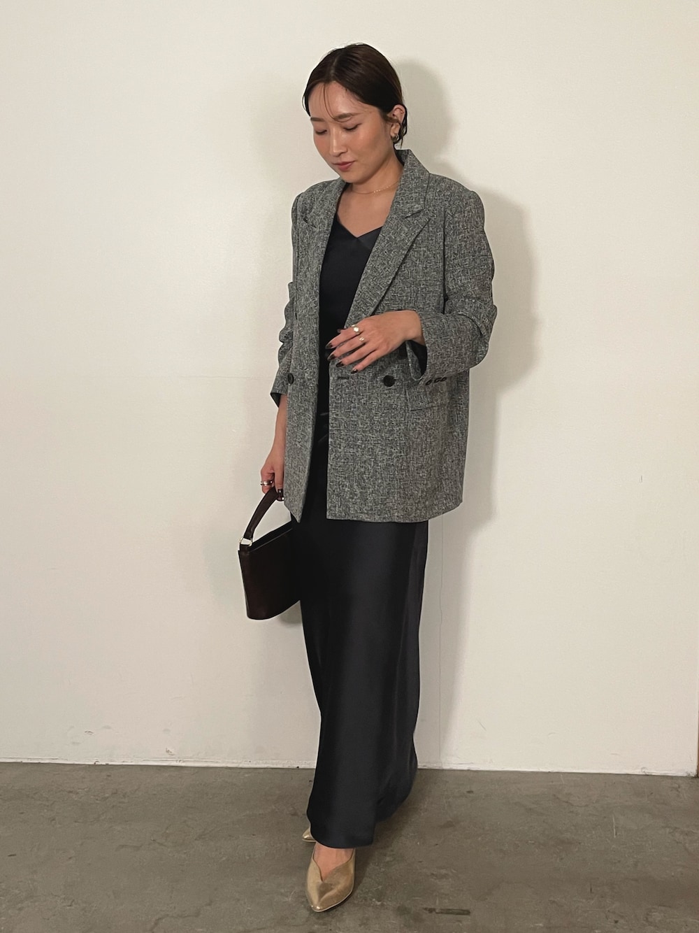 グレー系のドレス、ブラウン系のハンドバッグ、ゴールド系のパンプスを着用したレディースの冬コーディネートの1枚目の写真