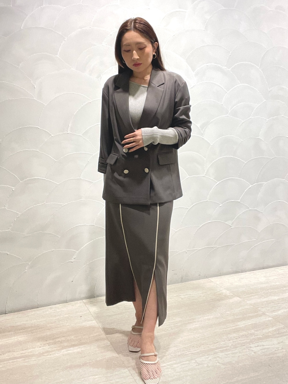 グレー系のスカート、ホワイト系のサンダル、グレー系のニット/セーターを着用したレディースの春コーディネートの1枚目の写真