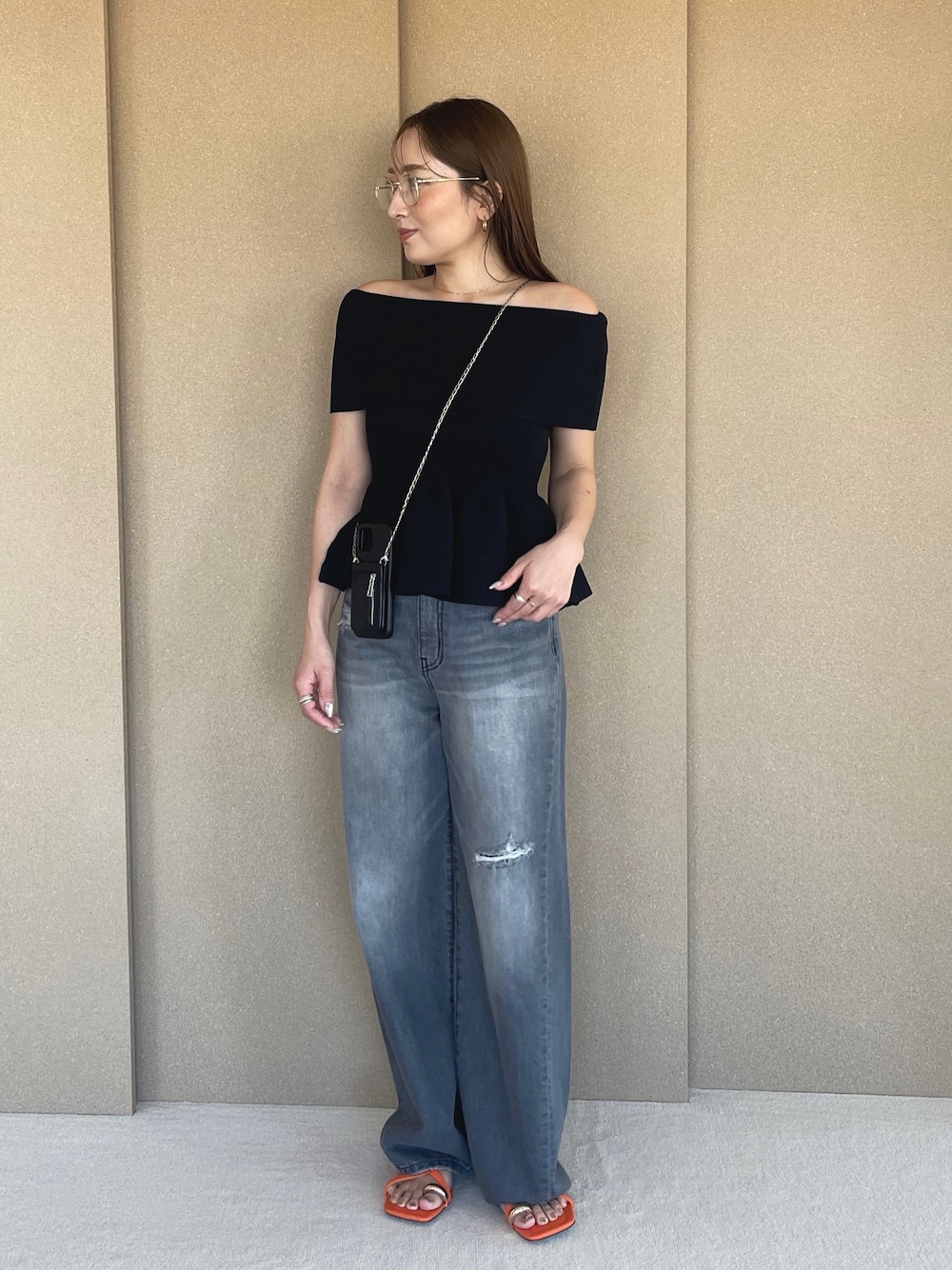 ブラック系のニット/セーター、グレー系のデニムパンツ、オレンジ系のサンダルを着用したレディースの春コーディネートの1枚目の写真