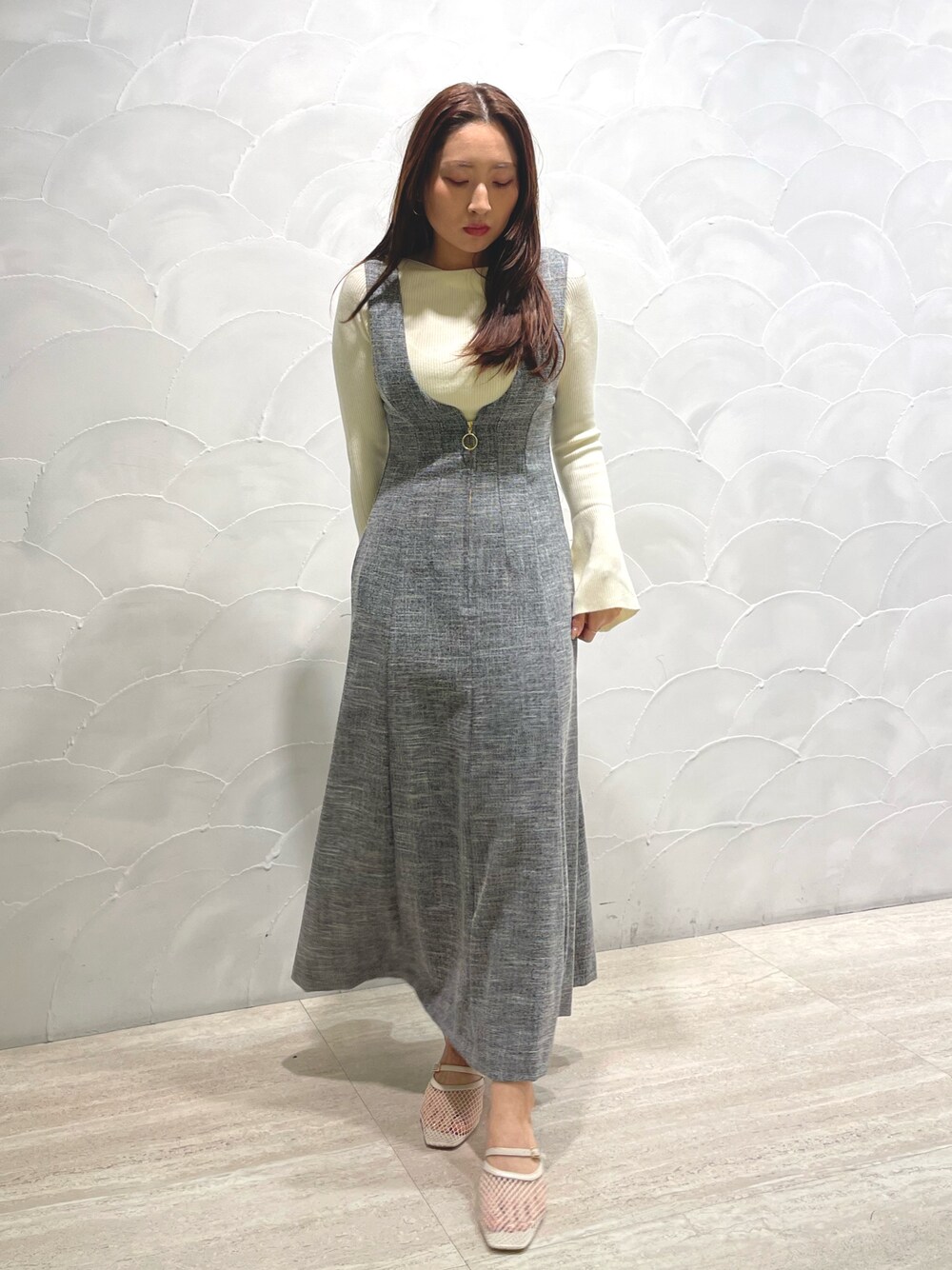 ホワイト系のサンダル、ホワイト系のニット/セーター、グレー系のジャンパースカートを着用したレディースの春コーディネートの1枚目の写真