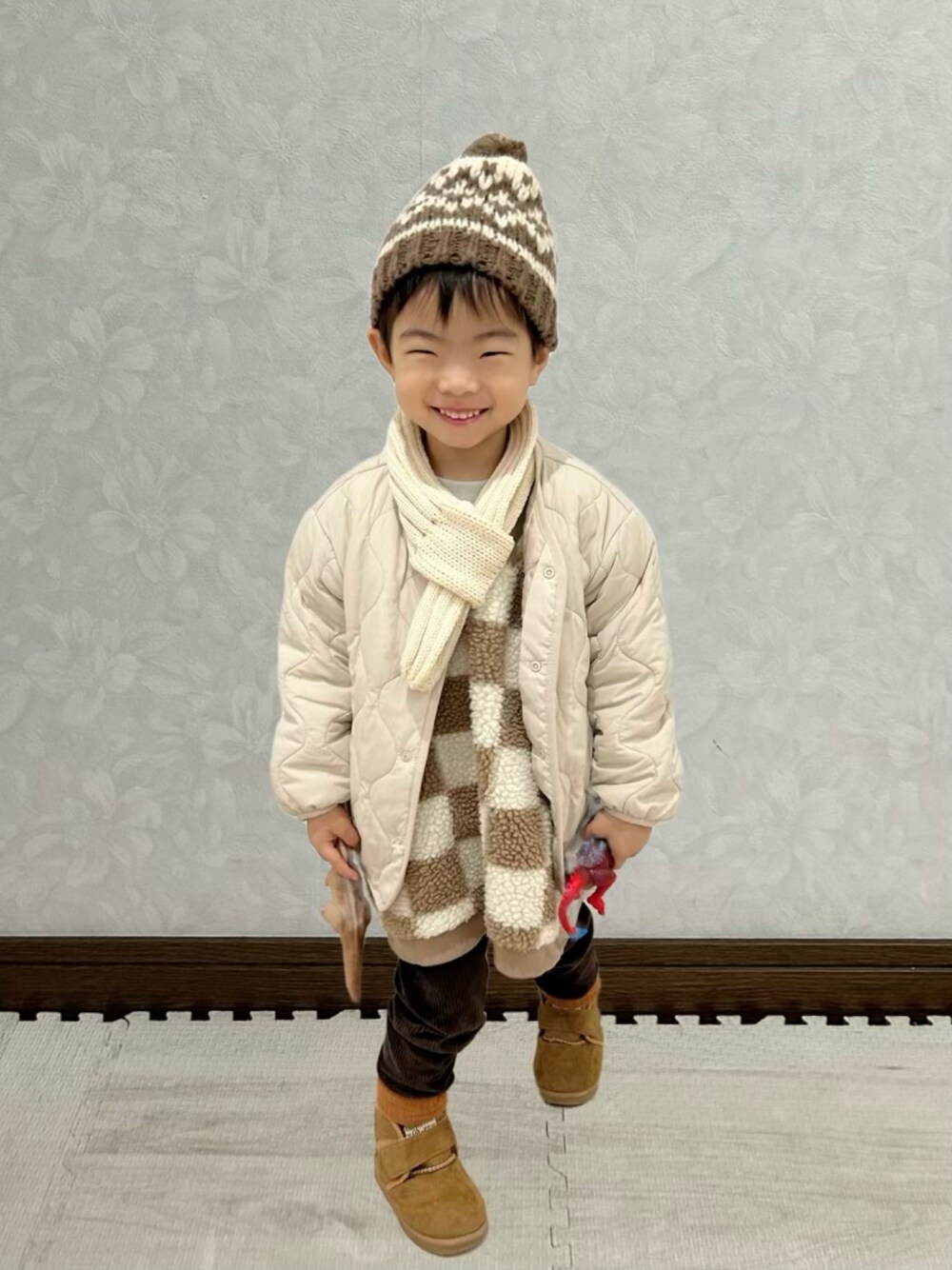 ブラウン系のベスト、ホワイト系のノーカラージャケット、ブラウン系のブーツを着用したキッズの冬コーディネートの1枚目の写真