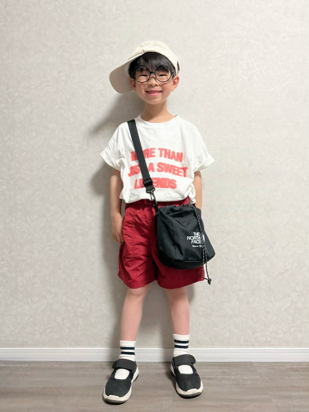 ブラック系のショルダーバッグ、ホワイト系のTシャツ/カットソー、レッド系のパンツを着用したキッズの春コーディネートの1枚目の写真