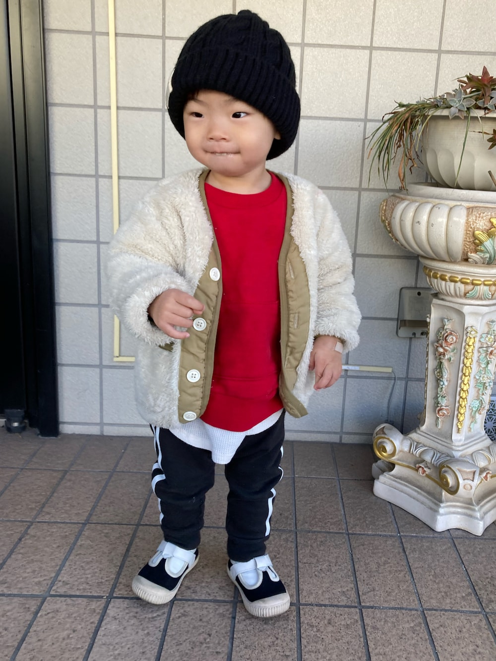 ベージュ系のノーカラージャケット、レッド系のスウェット、ブラック系のスウェットパンツを着用したキッズの冬コーディネートの1枚目の写真