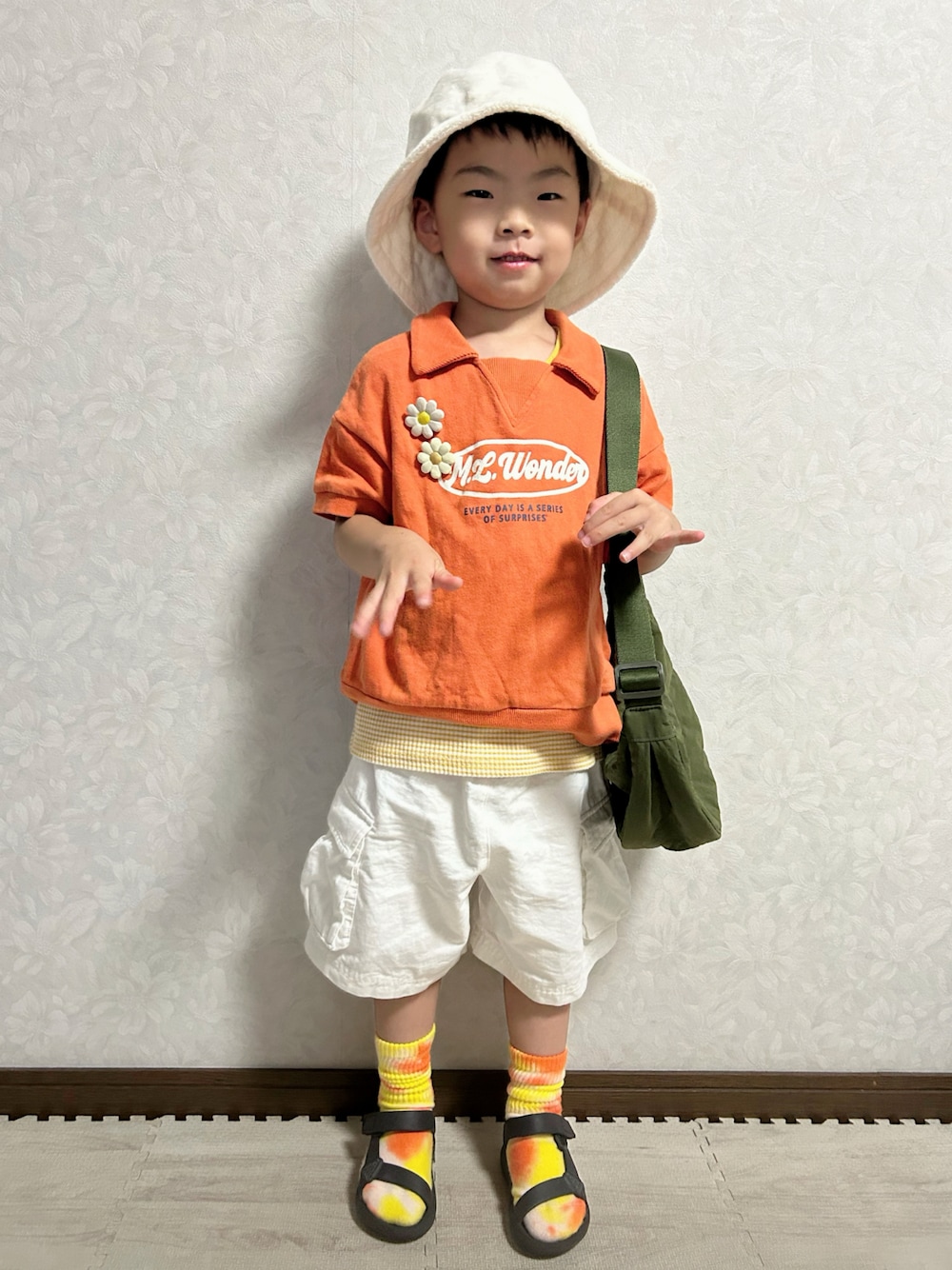オレンジ系のセットアップ、イエロー系のタンクトップ、グリーン系のショルダーバッグを着用したキッズの夏コーディネートの1枚目の写真