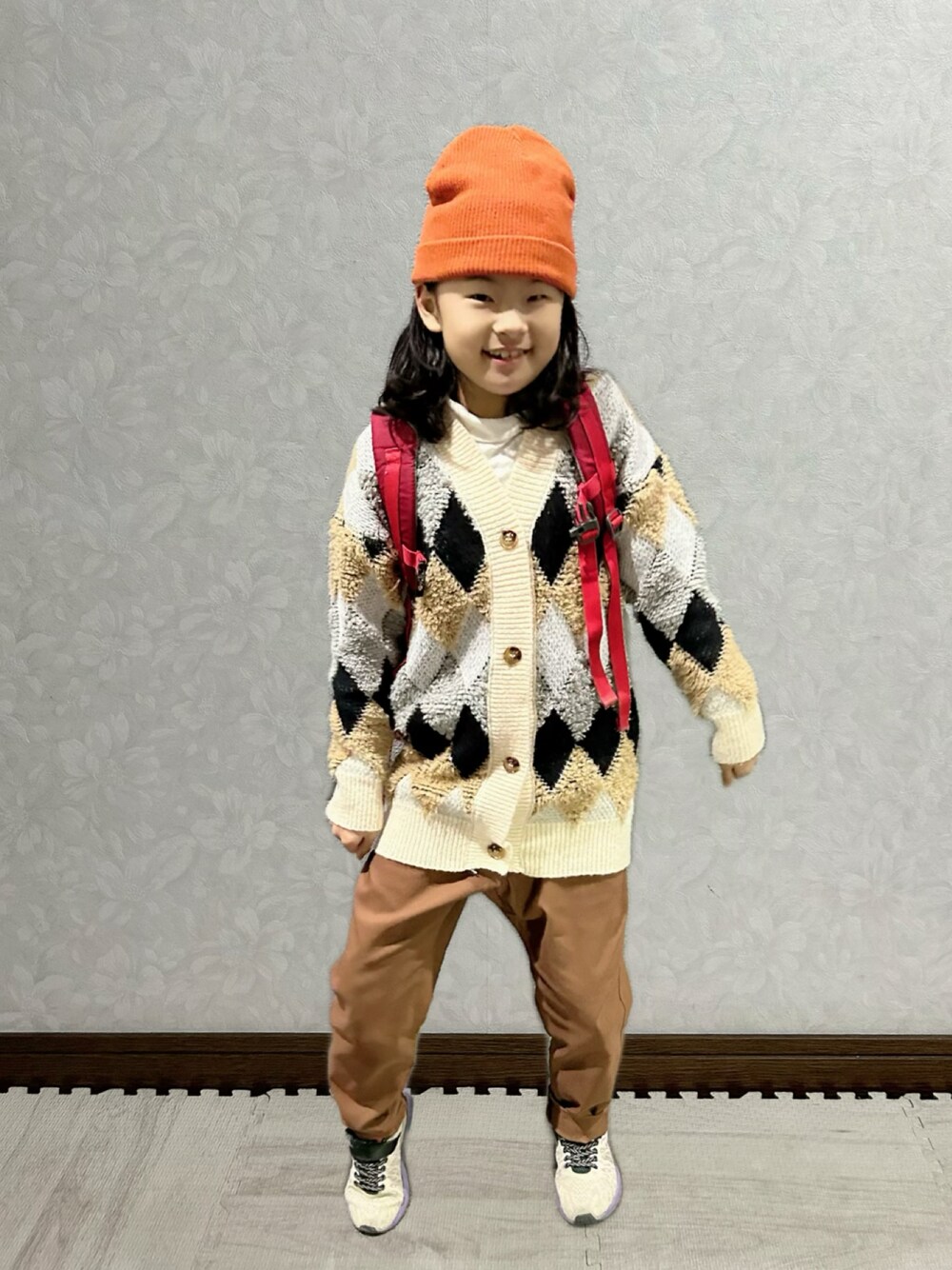 ホワイト系のTシャツ/カットソー、ベージュ系のカーディガン/ボレロ、レッド系のバックパック/リュックを着用したキッズの冬コーディネートの1枚目の写真