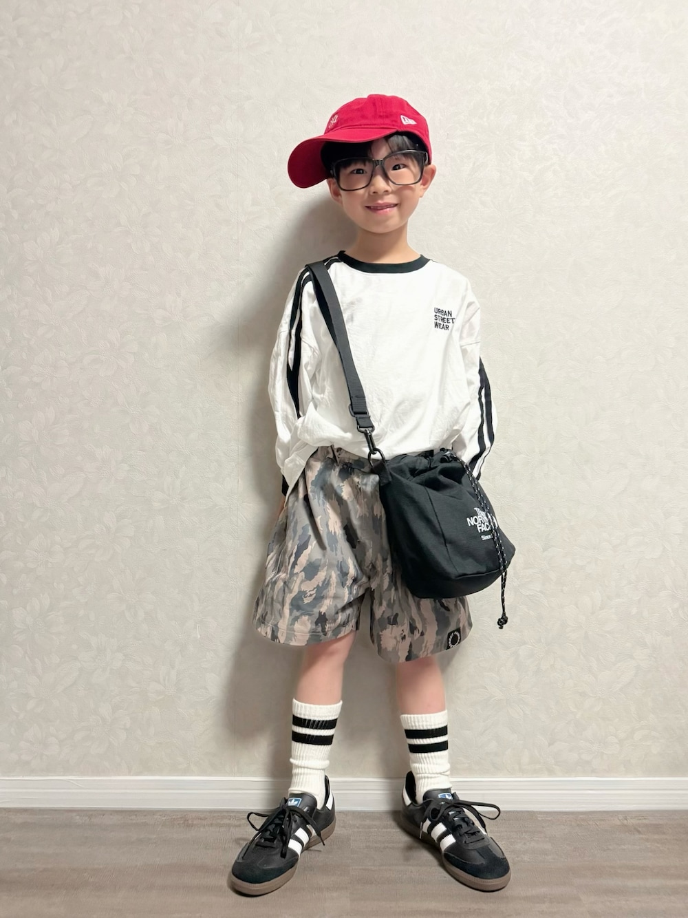 ブラック系のショルダーバッグ、ブラック系のスニーカー、ホワイト系のTシャツ/カットソーを着用したキッズの春コーディネートの1枚目の写真
