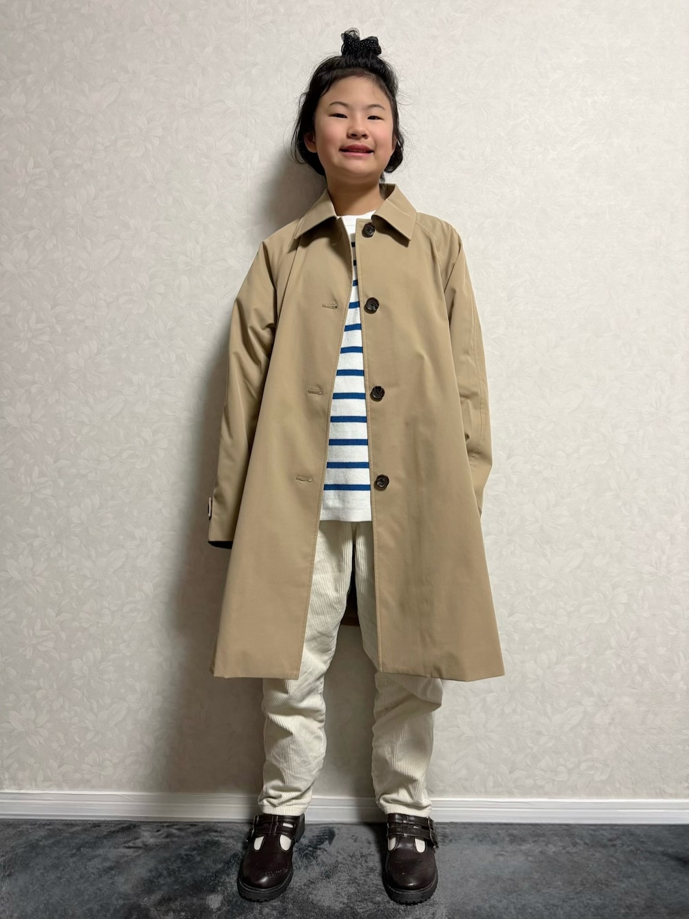 ブラウン系のその他シューズ、ホワイト系のニット/セーター、ベージュ系のステンカラーコートを着用したキッズの冬コーディネートの1枚目の写真