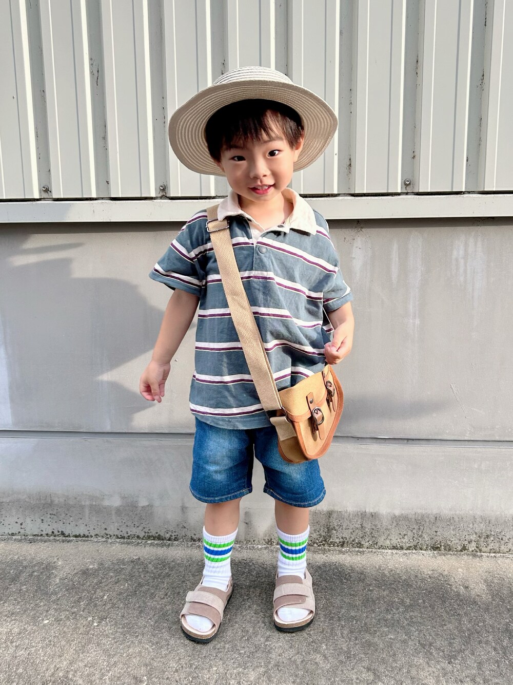 グリーン系のポロシャツ、ブラウン系のショルダーバッグ、ブルー系のデニムパンツを着用したキッズの夏コーディネートの1枚目の写真