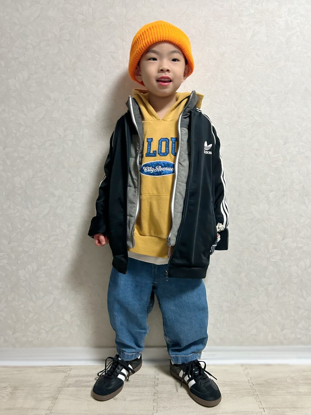 イエロー系のパーカー、グレー系のダウンベスト、ブラック系のジャージを着用したキッズの冬コーディネートの1枚目の写真