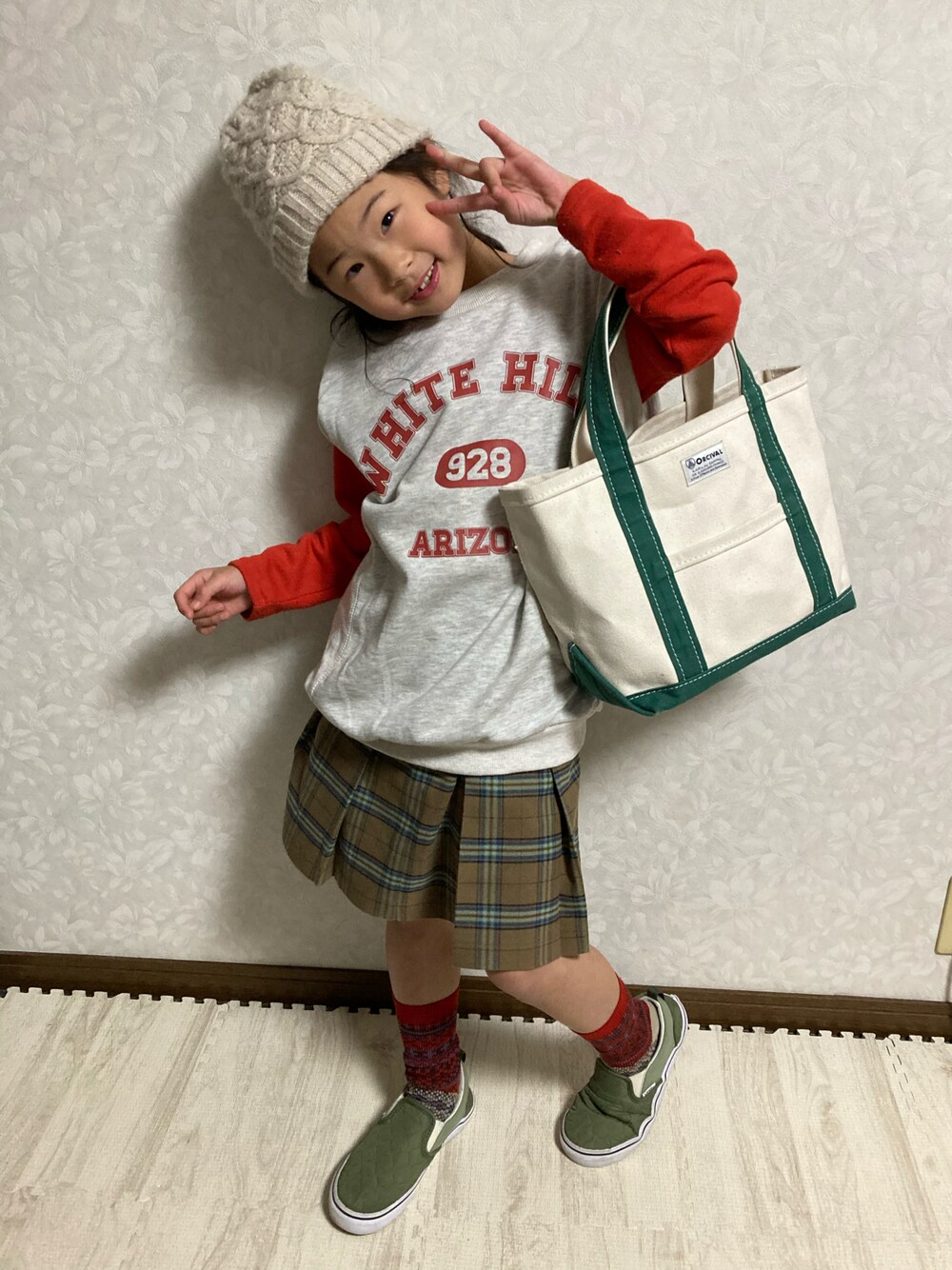 グレー系のベスト、ブラウン系のスカート、グリーン系のトートバッグを着用したキッズの冬コーディネートの1枚目の写真