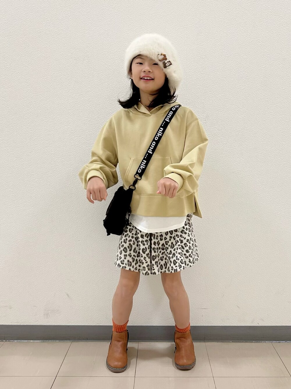 イエロー系のパーカー、ブラック系のショルダーバッグ、ベージュ系のスカートを着用したキッズの冬コーディネートの1枚目の写真
