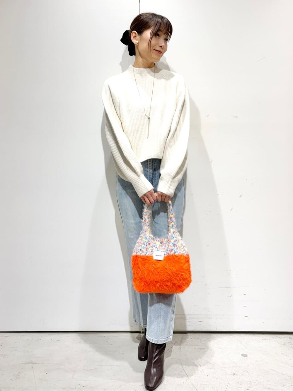 ホワイト系のニット/セーター、ブルー系のデニムパンツ、オレンジ系のトートバッグを着用したレディースの冬コーディネートの1枚目の写真