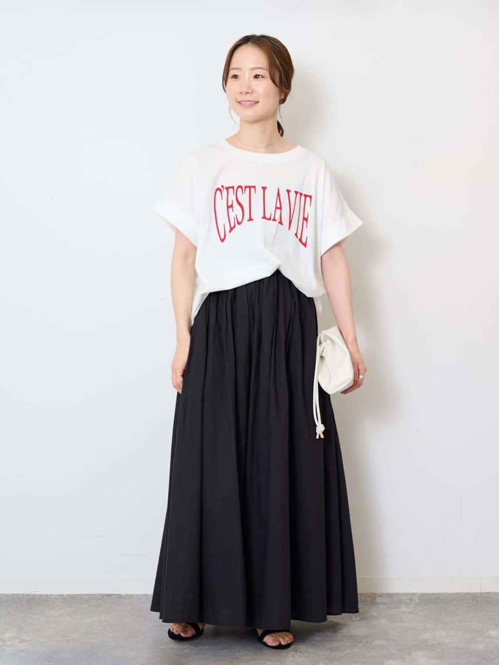 ブラック系のスカート、ホワイト系のTシャツ/カットソー、ホワイト系のクラッチバッグを着用したレディースの夏コーディネートの1枚目の写真