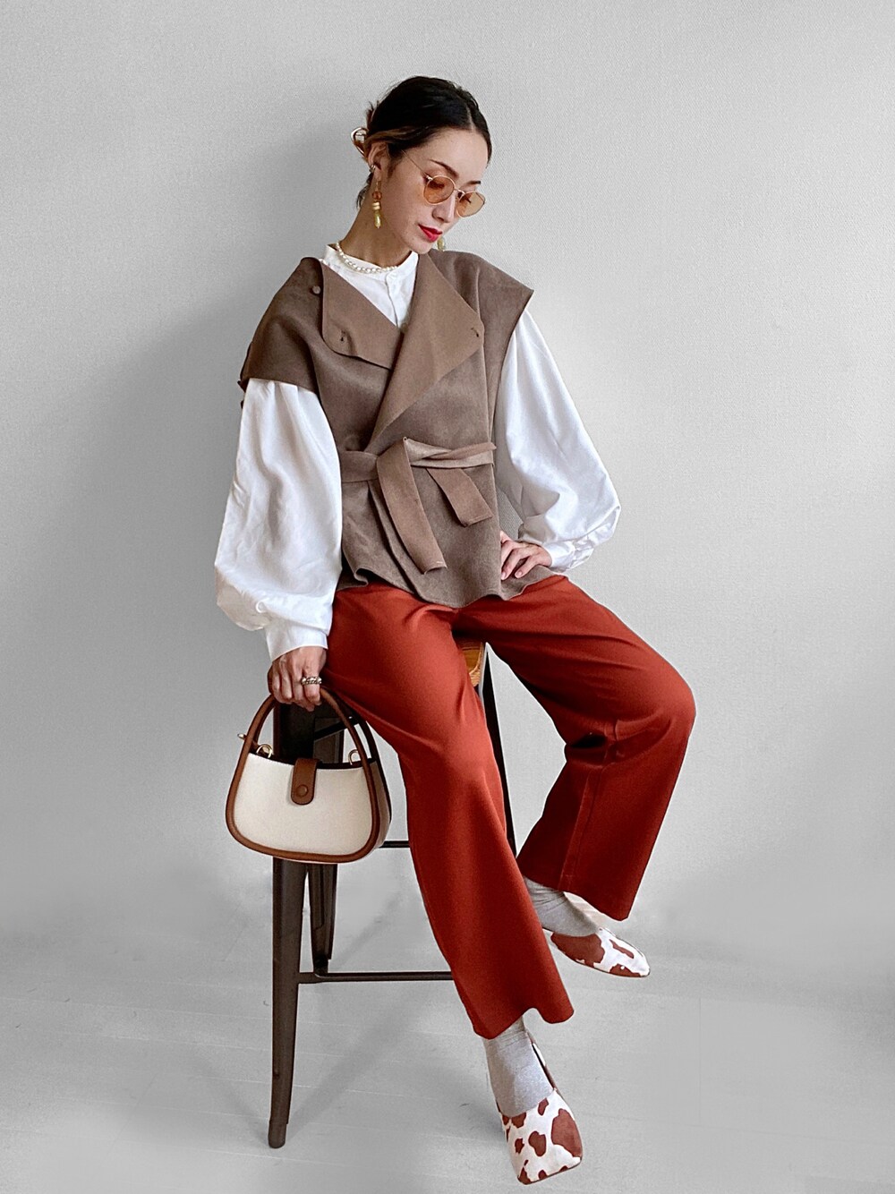 ベージュ系のベスト、ホワイト系のシャツ/ブラウス、ブラウン系のショルダーバッグを着用したレディースの秋コーディネートの1枚目の写真