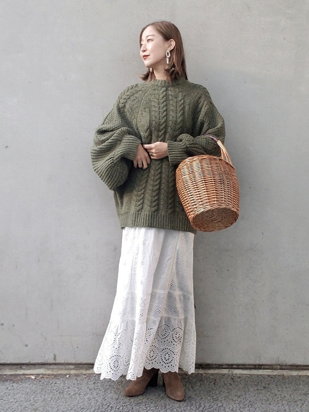 グリーン系のニット/セーター、ホワイト系のスカート、ベージュ系のかごバッグを着用したレディースの冬コーディネートの2枚目の写真