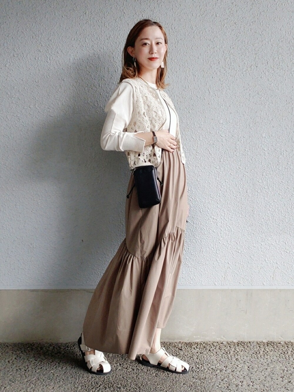 ブラック系のベスト、ホワイト系のワンピース、ブラック系の財布を着用したレディースの春コーディネートの3枚目の写真