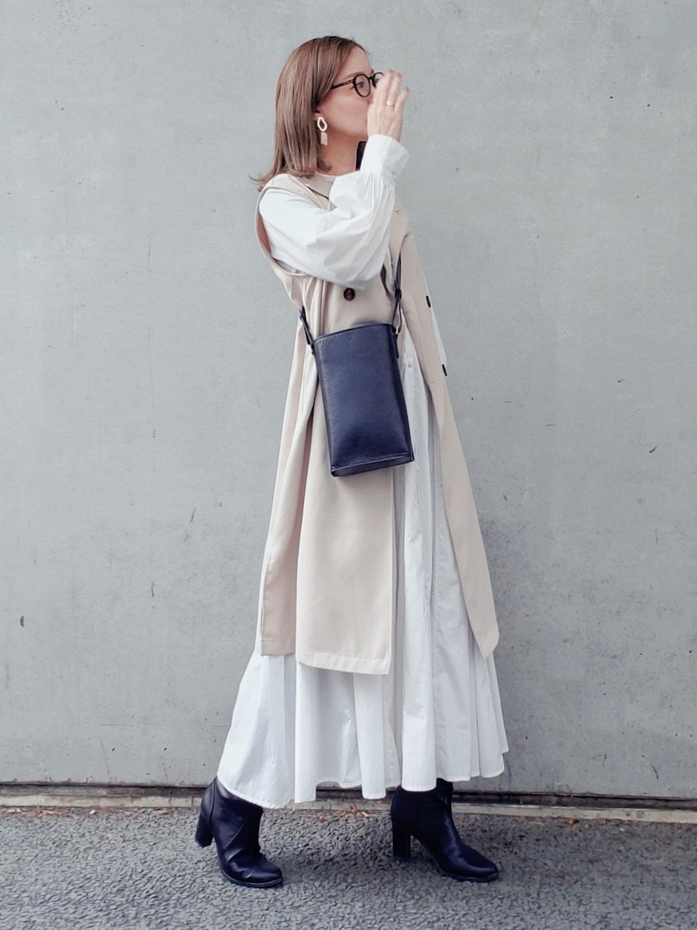 ブラック系のバッグ、ホワイト系のシャツワンピース、ブラック系のブーツを着用したレディースの春コーディネートの2枚目の写真