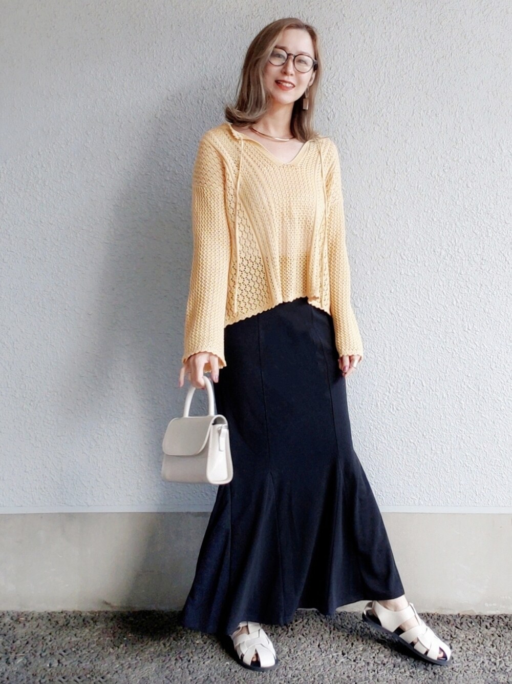 イエロー系のトップス、ブラック系のスカート、ホワイト系のサンダルを着用したレディースの春コーディネートの2枚目の写真