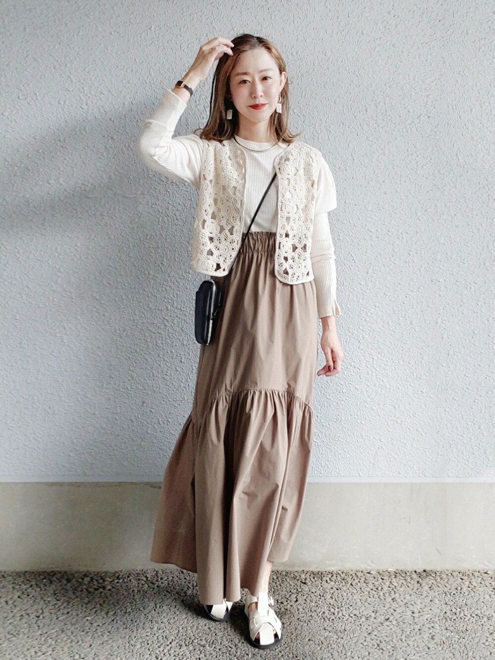 ブラック系のベスト、ホワイト系のワンピース、ブラック系の財布を着用したレディースの春コーディネートの2枚目の写真